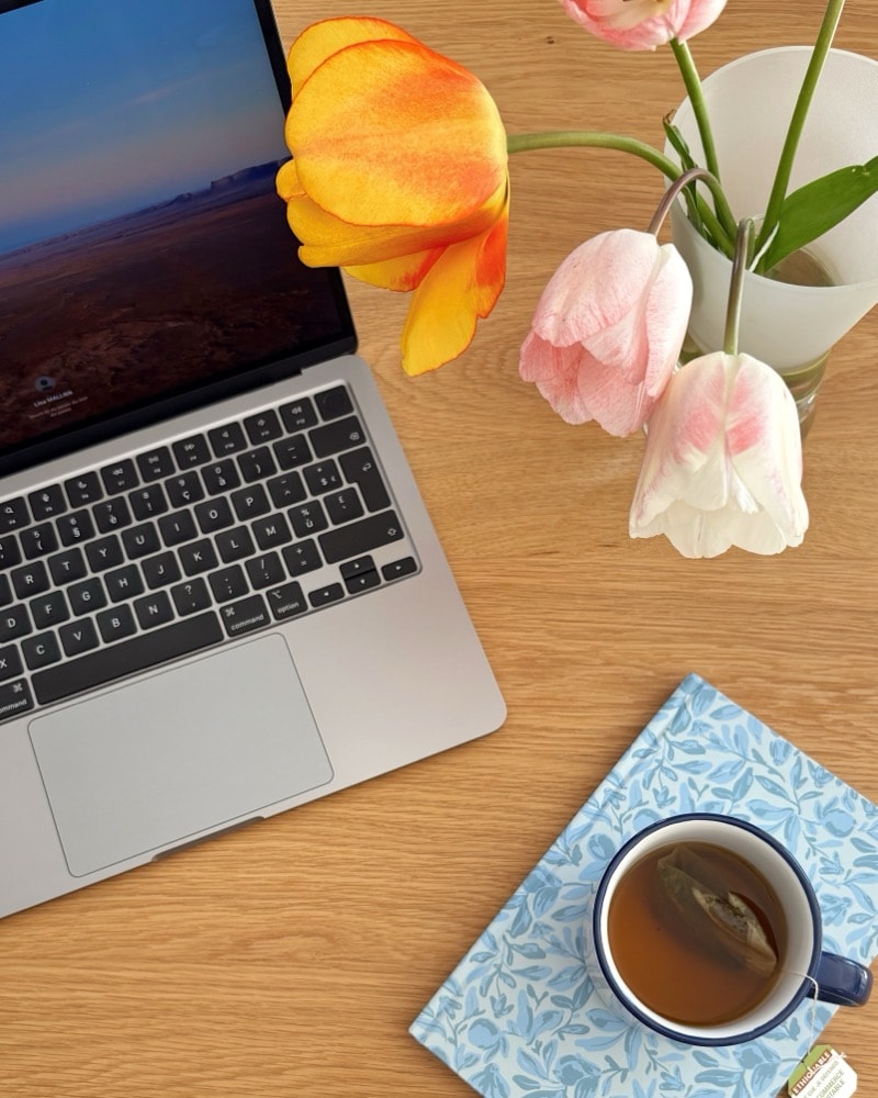 Vu de dessus : un ordinateur portable ouvert, un bouquet de tulipes et une tasse de thé posée sur un carnet.