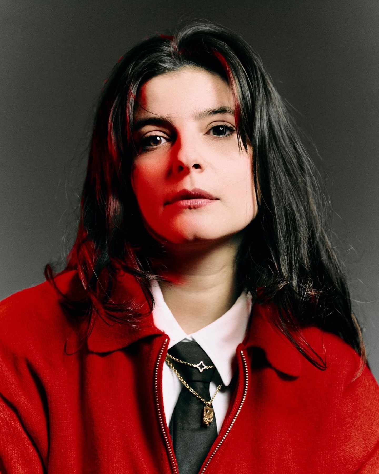 Portrait d’Akaëm en veste rouge sur fond gris.