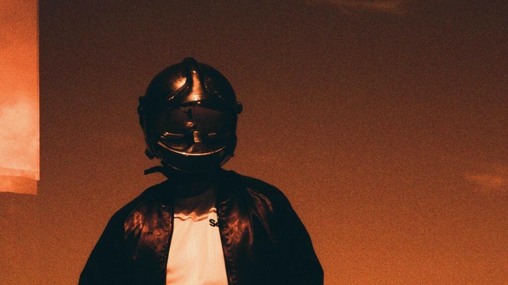 Silhouette casquée en veste de cuir devant un fond orangé.