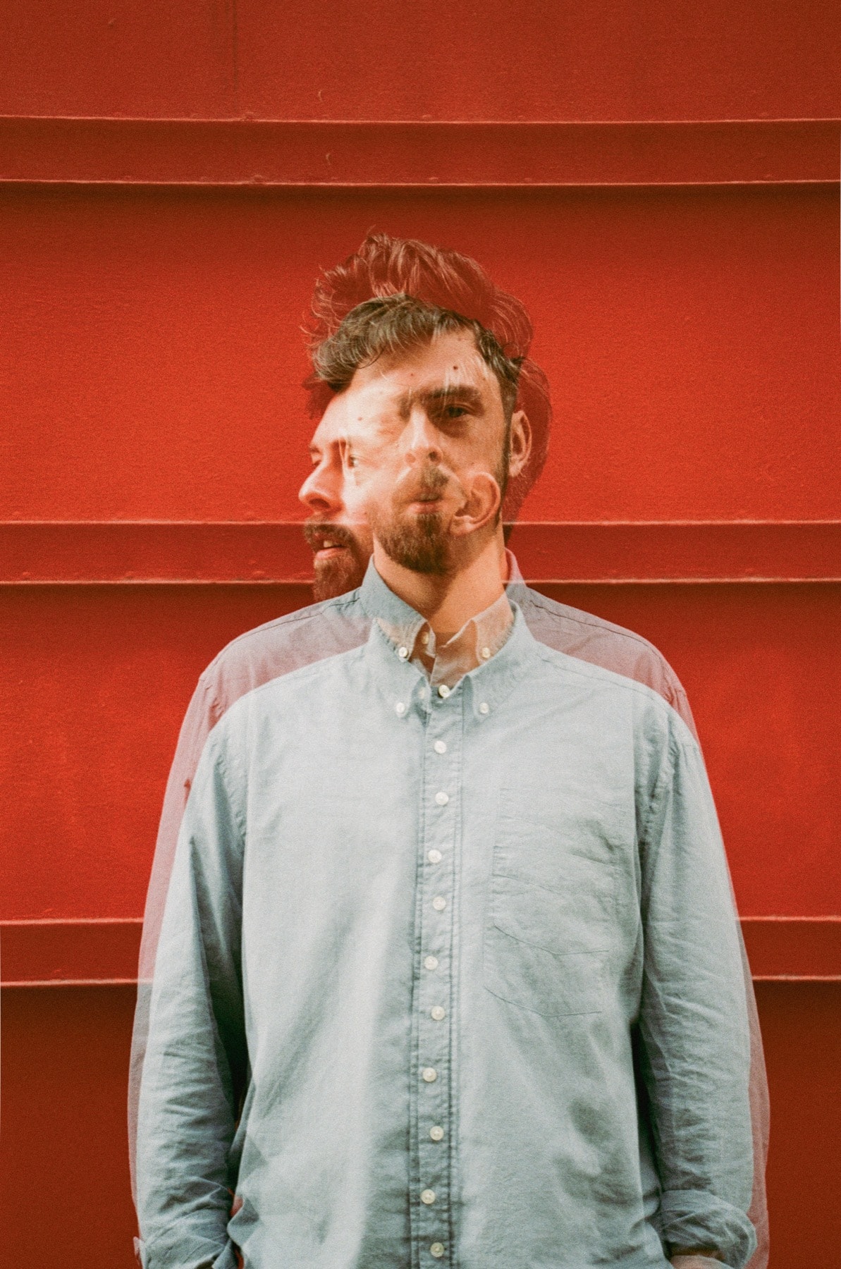 Paul Roman en chemise claire devant une paroi rouge, portrait en double exposition.